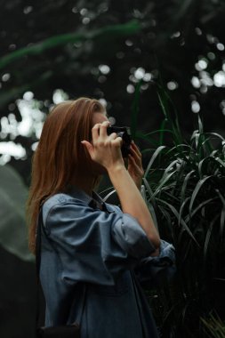 Botanik bahçesinde fotoğraf makinesi olan güzel bir genç turist kız. Bitkiler ve doğa..
