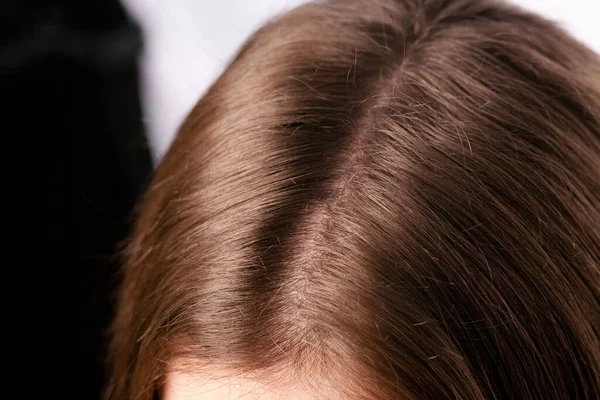 Close-up of female parting hair roots top view.