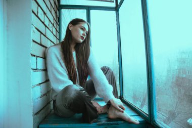Balkonda poz veren güzel, genç ve seksi bir kız. Modern tarzda bir kızın resim portresi. Oturmuş ve fotoğrafa ses eklemiş..