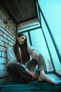 Balkonda poz veren güzel, genç ve seksi bir kız. Modern tarzda bir kızın resim portresi. Oturmuş ve fotoğrafa ses eklemiş..