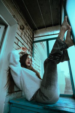 Balkonda poz veren güzel, genç ve seksi bir kız. Modern tarzda bir kızın resim portresi. Oturmuş ve fotoğrafa ses eklemiş..