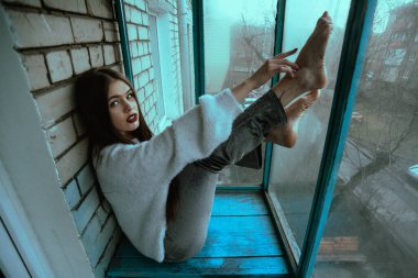 Balkonda poz veren güzel, genç ve seksi bir kız. Modern tarzda bir kızın resim portresi. Oturmuş ve fotoğrafa ses eklemiş..