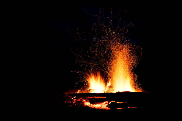 Beautiful bonfire with red, yellow and orange spurts of flames and sparks in the form of tracks on a black background