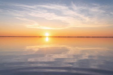 Güzel bulutlar, güneş, ufukta tren ve suda yansımalar olan tuzlu bir gölün üzerinde inanılmaz bir gün batımı. Bursol Gölü, Altai, Rusya.