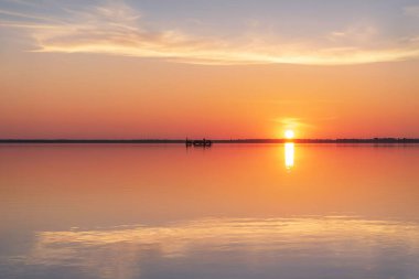 Güzel bulutlar, güneş, ufukta tren ve suda yansımalar olan tuzlu bir gölün üzerinde inanılmaz bir gün batımı. Bursol Gölü, Altai, Rusya.