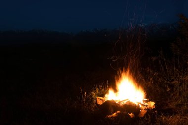 Güzel bir kamp ateşi ve karlı dağların arka planında kıvılcımlar saçan gece manzarası.