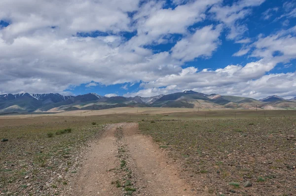 Een onverharde weg steppe op een achtergrond van bergen, de lucht en de wolken — Stockfoto