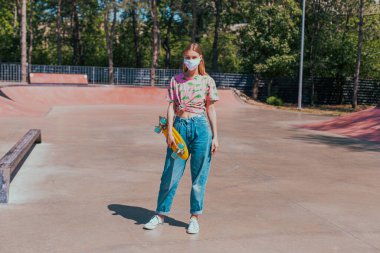 Dışarıda, şehir kaykay parkında, zarif bayan Asyalı kameranın önünde yaratıcı koruyucu bir maskeyle bakıyor. Covid-19 'un düz konseptine bakıyor.