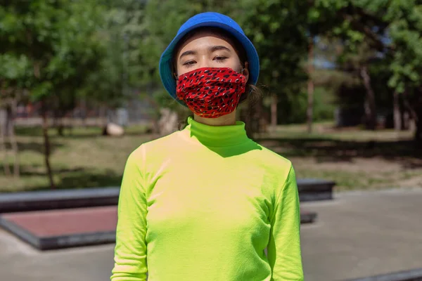Na zewnątrz, w miejskim skateparku, stylowa kobieta azjatka, patrząc z kreatywną maską ochronną przed kamerą, patrząc prosto na koncepcję Covid-19 — Zdjęcie stockowe