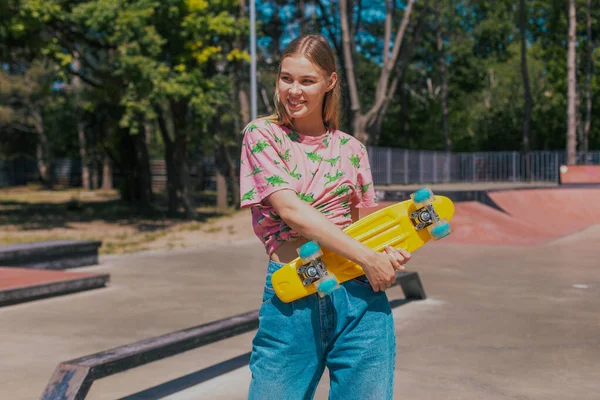 스케이트보드 를 들고 있는 현대인 스케이트 공원에서 아름다운 미소를 짓고 있는 놀라운 금발의 여자가 히프 스터 복장을 하고 있어서 행복하다. — 스톡 사진