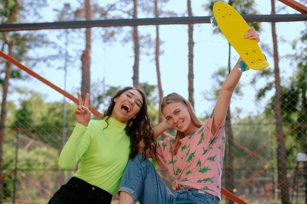 Dos chicas divirtiéndose juntas con skate board. Dos hermosas y jóvenes novias divirtiéndose con un monopatín —  Fotos de Stock