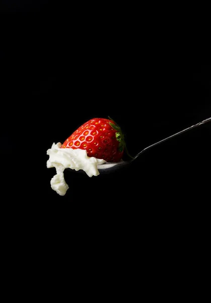 Crema batida y una fresa en una cuchara de plata sobre fondo negro — Foto de Stock