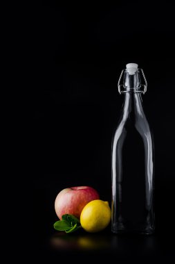 Boş cam şişe, elma ve limon siyah arka plan üzerine