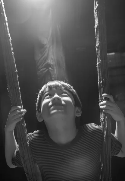 Маленький мальчик играет качели крытый край света черно-белый — стоковое фото
