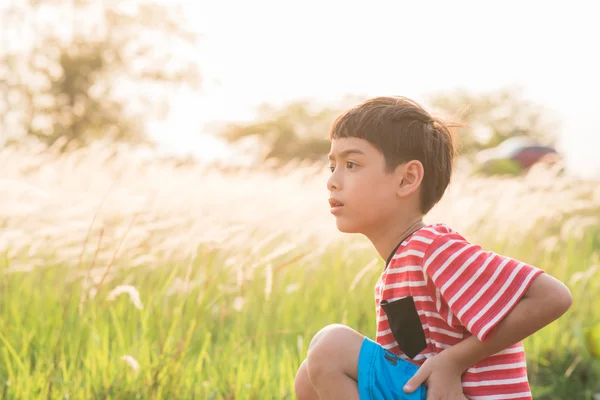 Petit garçon assis avec des herbes dorées champ coucher de soleil temps — Photo