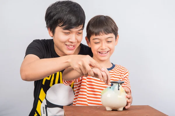 Asian teenager male sibling save the money into piggy bank — Stock Photo, Image