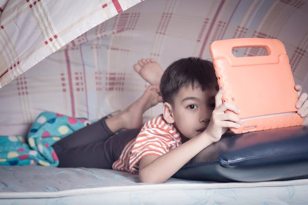 Menino insinuando sob blacket jogar tablet — Fotografia de Stock