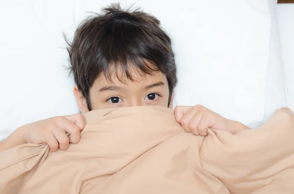 Pequeño niño acostado en la cama con la manta cubierta media cara —  Fotos de Stock