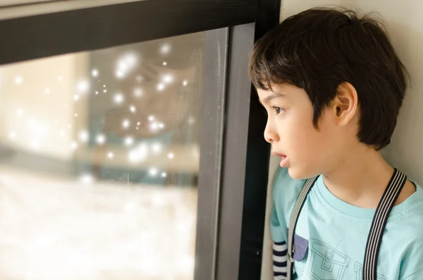 Kleine jongen op zoek naar sneeuw buiten venster — Stockfoto