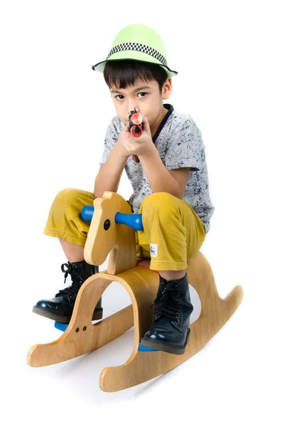 Menino pequeno tlaking cavalo de madeira com brinquedo arma no fundo branco — Fotografia de Stock