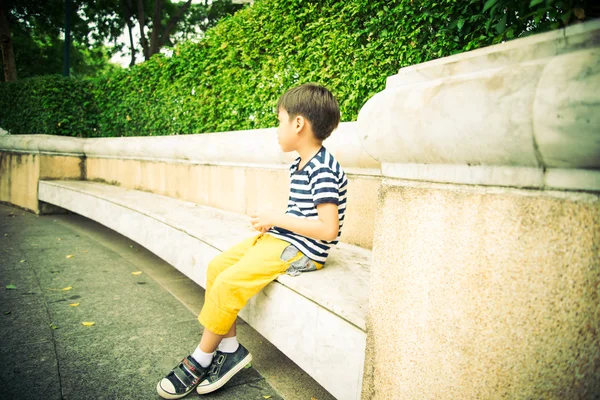 Kleiner Junge sitzt auf der Bank im Park — Stockfoto