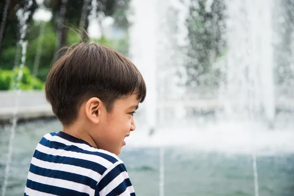 Liten pojke tittar på fontänen i parken — Stockfoto