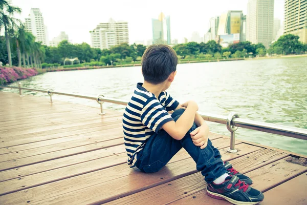 Маленький хлопчик сидить поруч з лагунним озером в парку — стокове фото