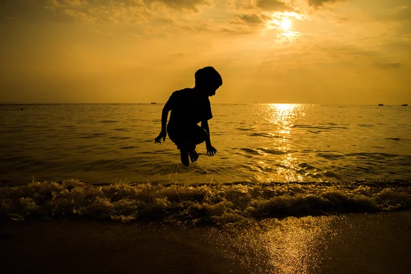 Silhueta de menino saltando sobre a onda de praia — Fotografia de Stock