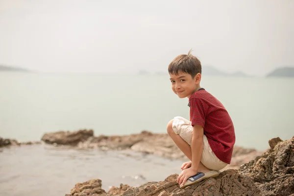 Petit garçon assis sur le rocher sur la plage — Photo