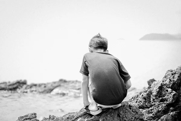 Küçük çocuk plaj siyah ve beyaz kayaya oturan — Stok fotoğraf