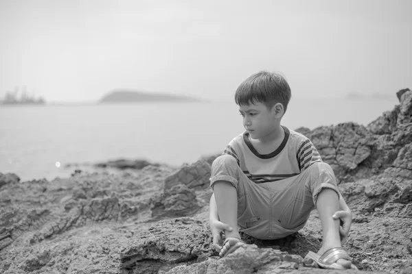 Liten pojke sitter på sten på stranden svart och vitt — Stockfoto
