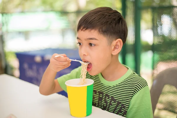 Маленький мальчик ест лапшу на открытом воздухе в парке — стоковое фото