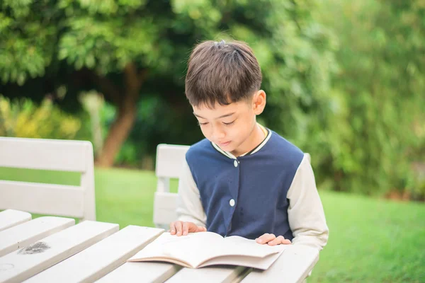 Petit garçon lisant un livre dans le parc — Photo