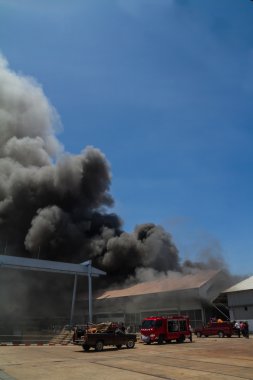 Burning warehouses with black smoke against blue sky