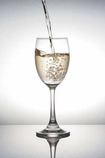 White wine pouring into wineglass on white background — Stock Photo, Image