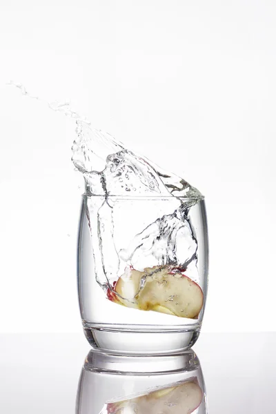 Apple pieces drop into a glass of water, make water splashing — Stock Photo, Image