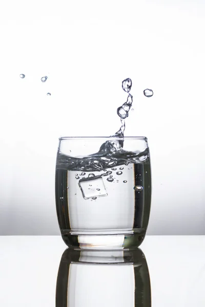 Ice dropping into a glass of water — Stock Photo, Image