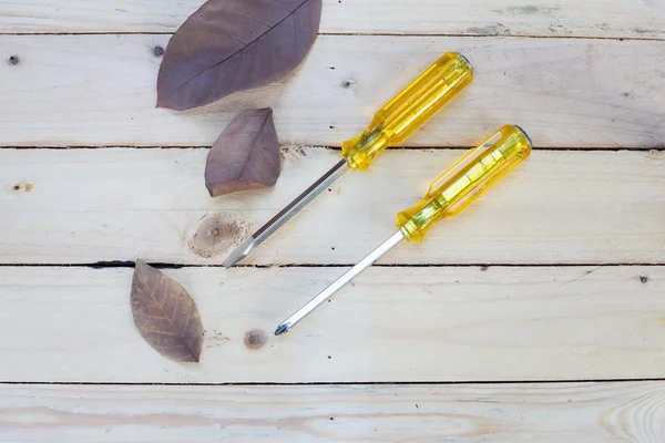 Tournevis jaune et feuilles séchées sur fond bois — Photo