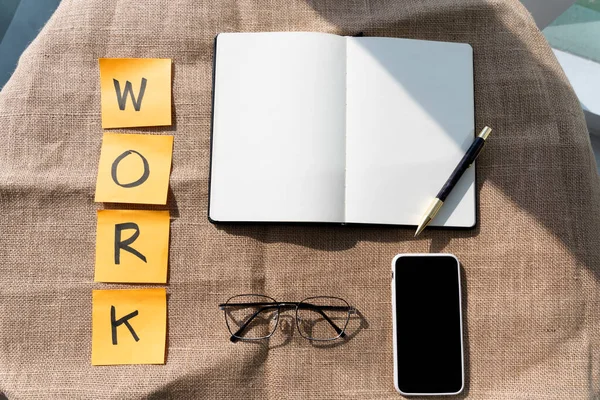 Desk of writer with pen, eyeglasses, and smartphone on brown table.