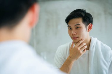 Asyalı genç adam banyo aynasında kendine bakıyor..