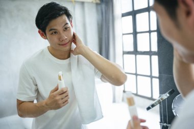 Asyalı genç adam banyodaki aynaya yüz kremi sür..