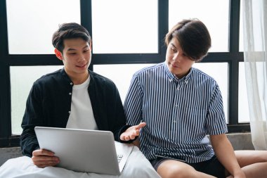 Birkaç Asyalı LGBTQ + adamı birlikte oturup dizüstü bilgisayar kullanırken konuşuyor..