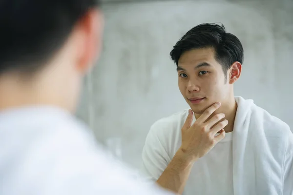 Asyalı genç adam banyo aynasında kendine bakıyor..