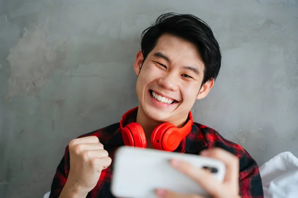 Asyalı genç adam yatak odasında akıllı telefondan mobil oyun oynamayı sever..