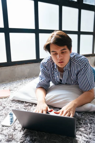在家里靠窗的笔记本电脑上工作的亚洲年轻人 — 图库照片