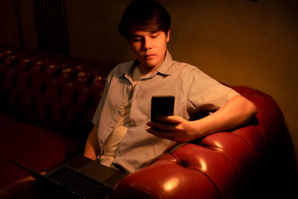 在沙发上使用智能手机和笔记本电脑的亚洲青年商人 — 图库照片
