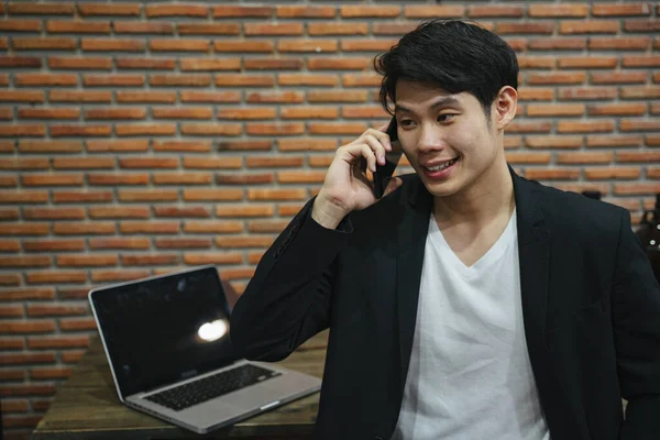 Asian young businessman talking on the phone in brick office.