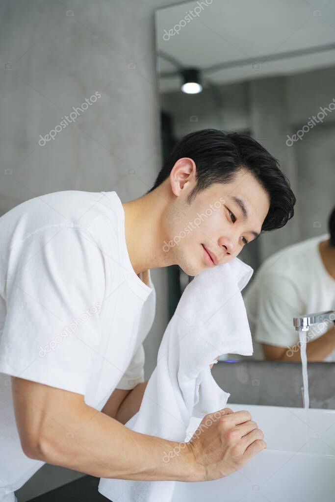Asian young man washing and cleaning face with towel in bathroom.