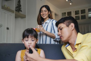 Asyalı anne, oturma odasında ailesine portakal suyu servis ediyor..