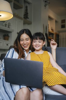 Asyalı anne-kız dizüstü bilgisayarda kanepe üzerinde film izliyorlar..